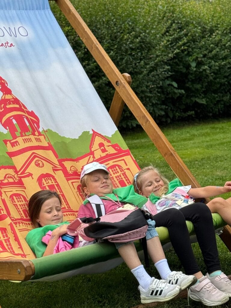 Bajkowa huśtawka z dziećmi odpoczywającymi w parku, z ilustracją renesansowego zamku na tle. Idealne dla dzieci, relaks i zabawa na świeżym powietrzu, promująca aktywność na zewnątrz i edukację historyczną.