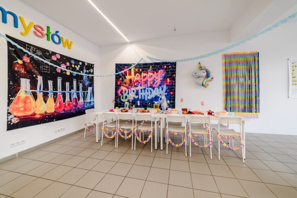 Kolorowa sala urodzinowa dla dzieci z jednorożcem, neonowym napisem "Happy Birthday" oraz dekoracjami w stylu fantazyjnym i tematycznym, idealna na przyjęcie dziecięce.