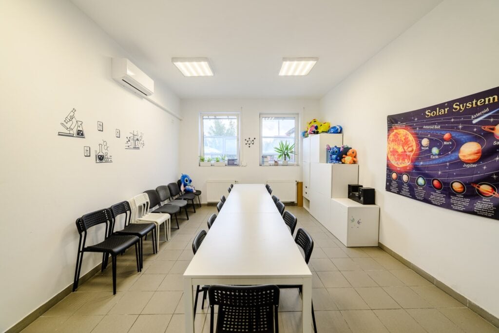 Przestronna sala edukacyjna z kolorowymi pluszakami, tabelą Układu Słonecznego i nowoczesnym wyposażeniem w centrum nauki i rozwoju dzieci.