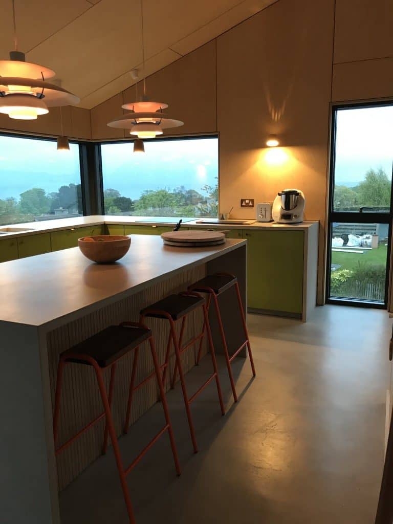 Bright kitchen with large windows, modern lighting, and sleek green cabinetry.