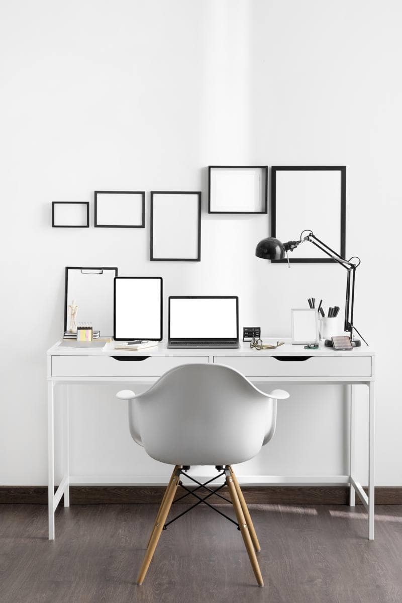 Minimalist office workspace with white desk, laptop, desk lamp, and organisational accessories.