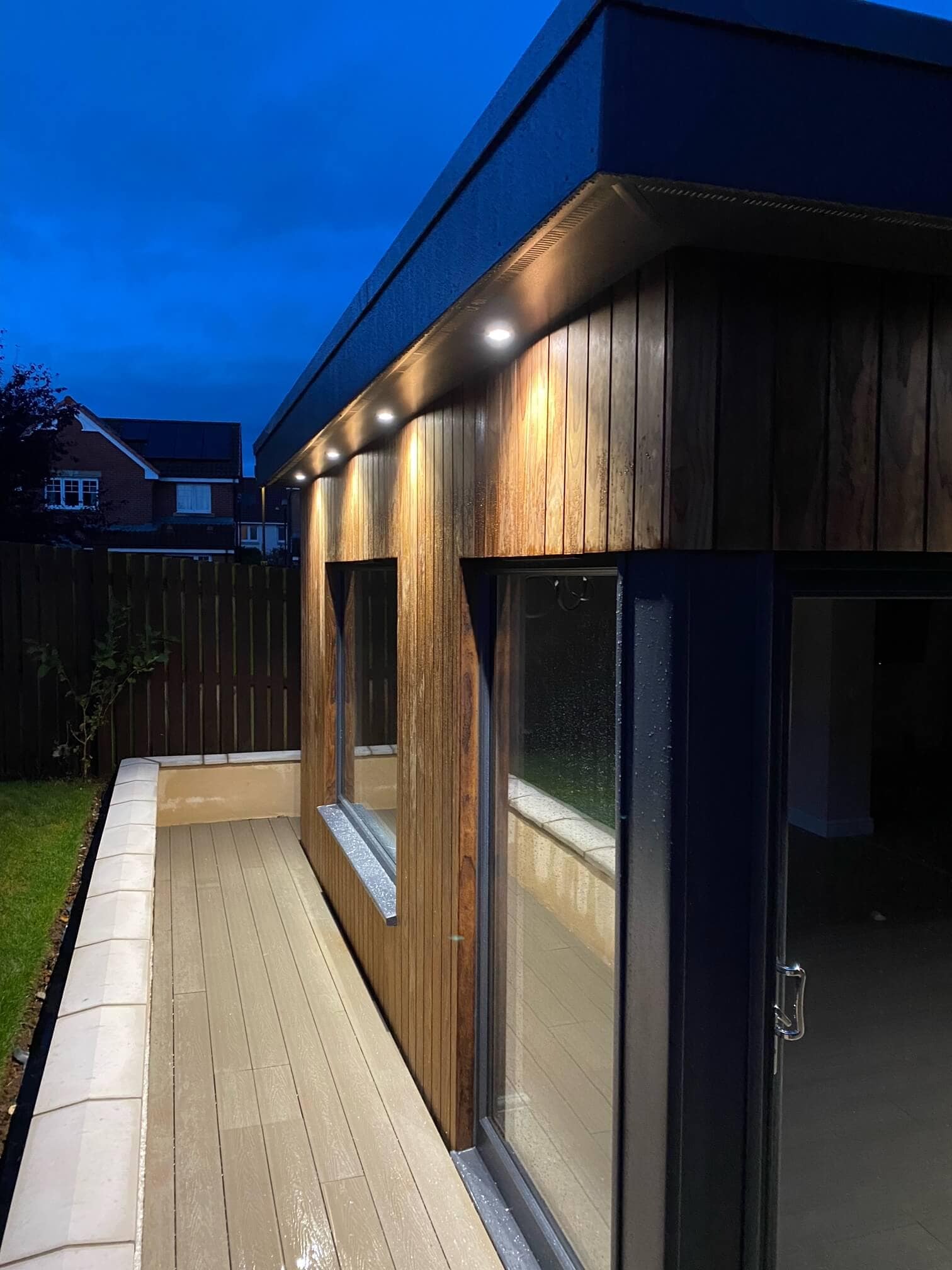 Lighted wooden paneling, large glass doors, outdoor decking, contemporary architecture.
