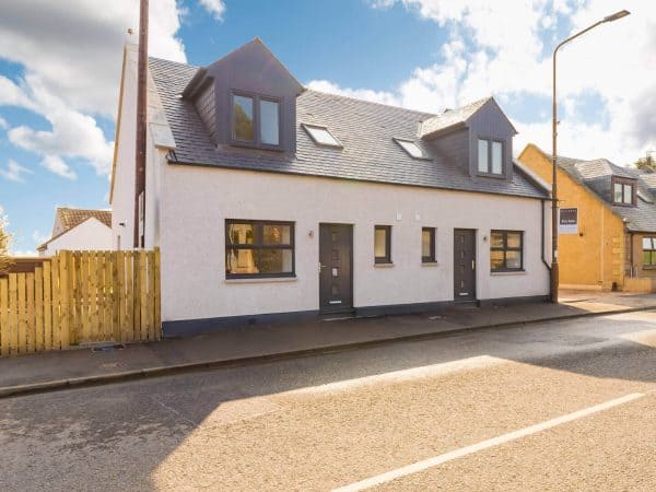 Stylish white duplex homes with black framed windows and modern entrance doors, situated on a quiet street in the UK.
