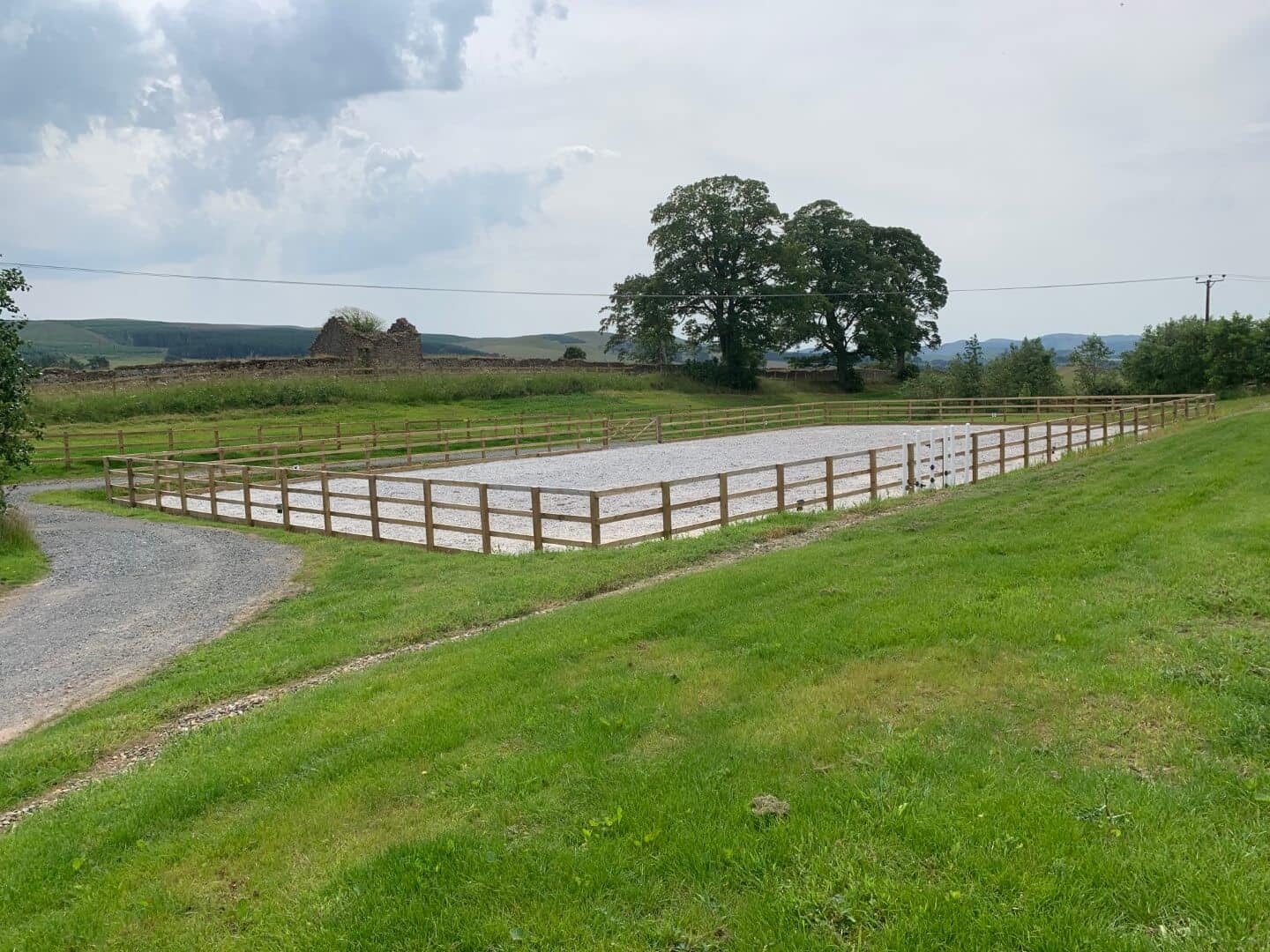 Equestrian riding arena with wooden rail fencing, set in lush rural countryside, ideal for outdoor horse riding.