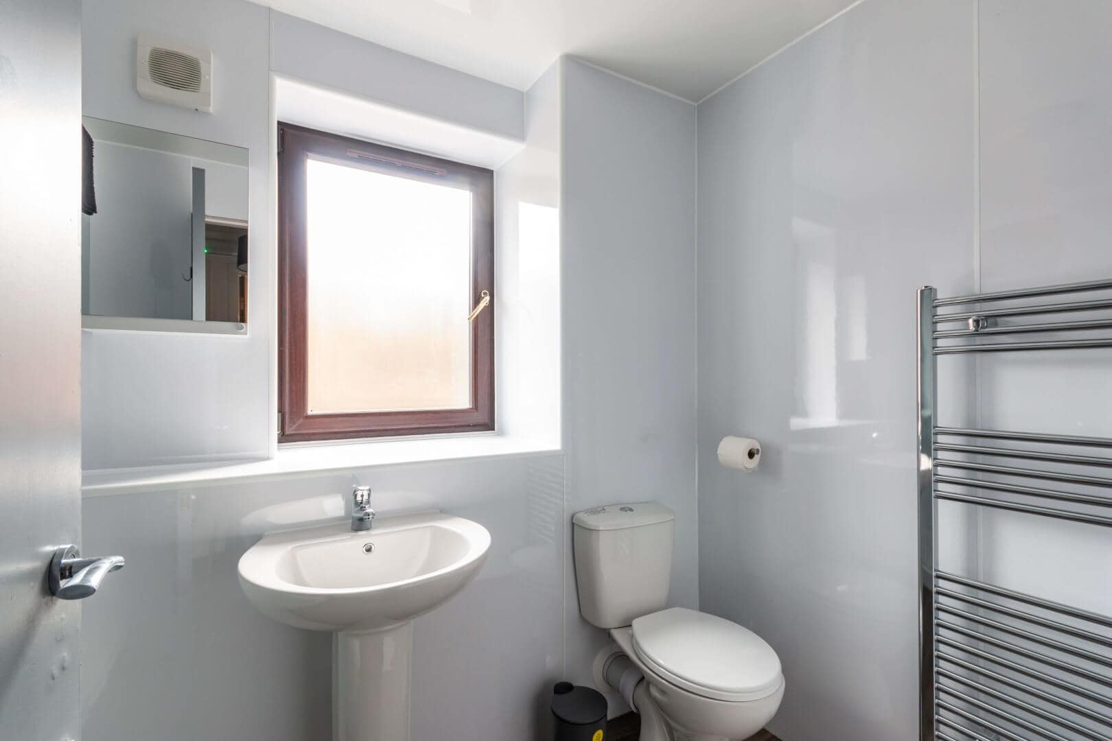 Bathroom interior featuring white sink, toilet, and natural light from wooden-framed window.