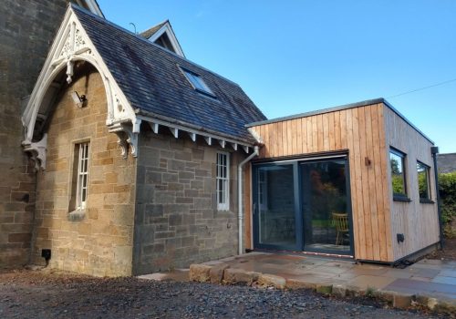Modern wooden house extension with large glass doors.