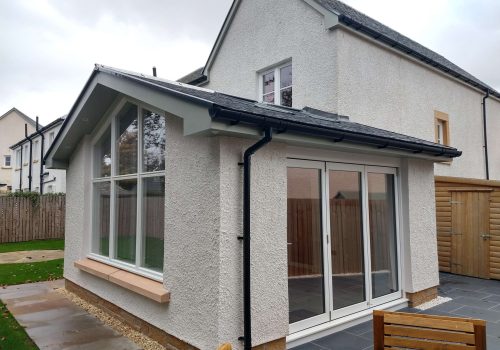 Bright home extension with large bay windows and sliding doors, blending indoor and outdoor living spaces seamlessly.