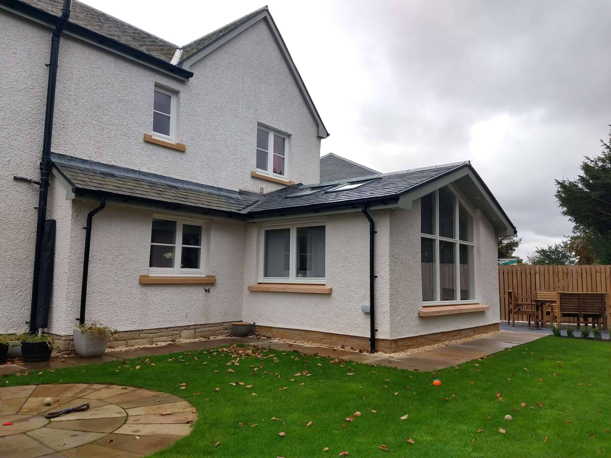 Spacious white textured house exterior with large windows and a sunny backyard, ideal for family living and outdoor entertaining.