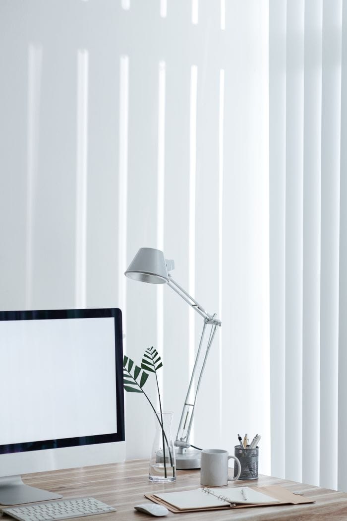 Minimalist home office with computer, desk lamp, and decorative plants, bright natural lighting.