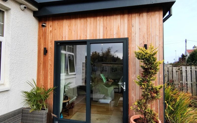 Modern garden room with wooden exterior and large glass doors, ideal for outdoor entertaining and relaxation.