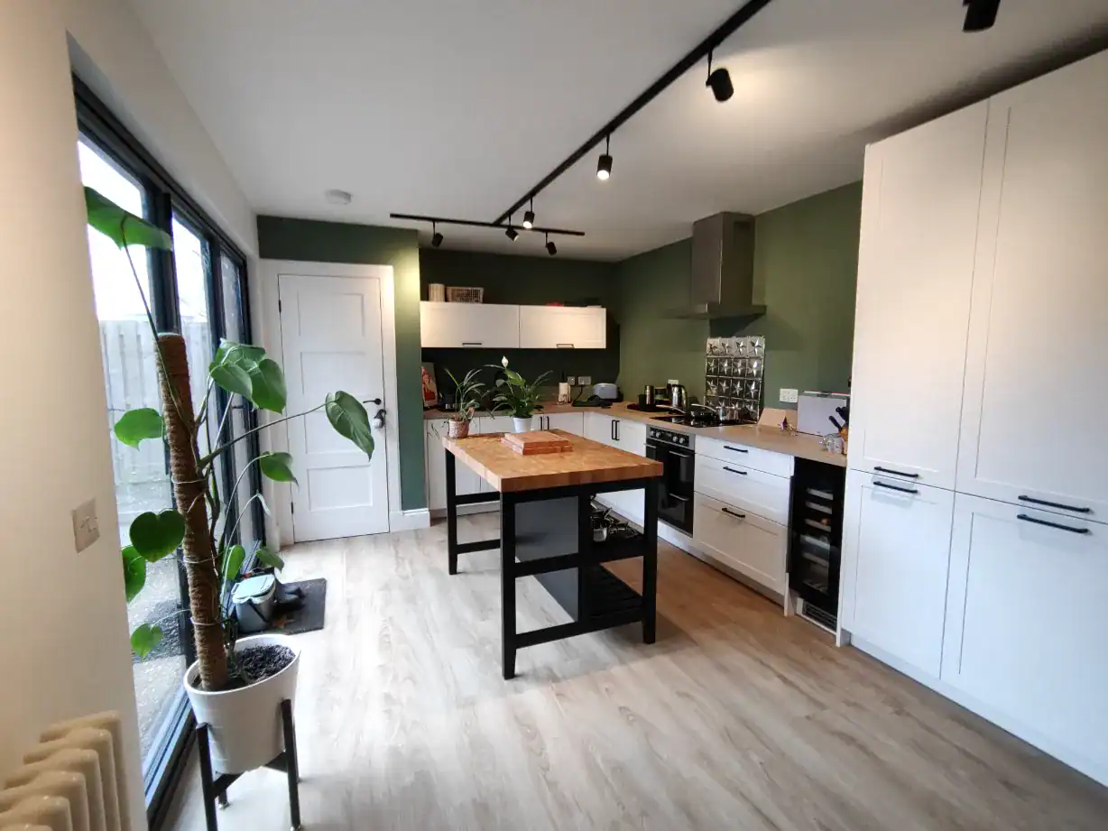 Bright modern kitchen with white cabinets, green accent wall, and central wooden island, perfect for contemporary home living.