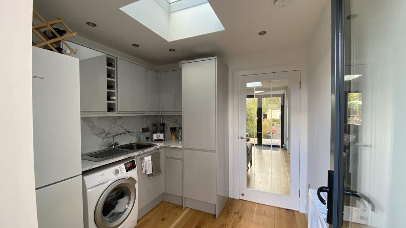 Bright contemporary kitchen with skylight, white cabinets, marble backsplash, and integrated appliances.