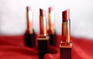 Four red lipsticks arranged on a red fabric background.