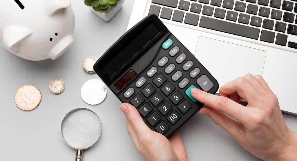Calculator on white desk with bitcoin coins, magnifying glass, and laptop, representing financial planning, digital currency, and business analysis for SEO optimization.