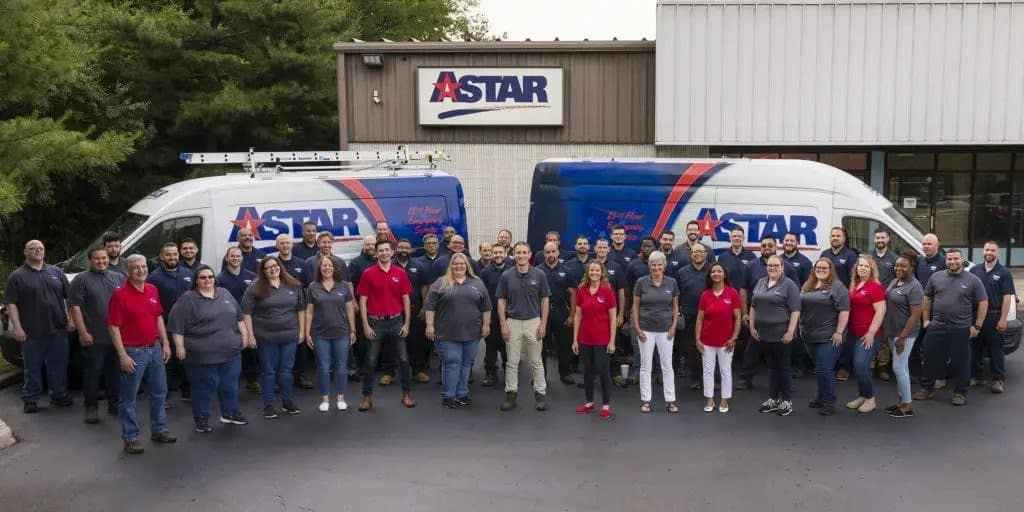 A group of people wearing red and gray shirts stand in front of two Astar-branded vans outside a building with an Astar sign.