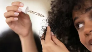 Une femme applique un sérum avec une pipette sur ses cheveux bouclés, un soin pour la porosité des cheveux.