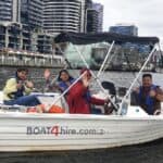 Group enjoying a boat ride on Melbourne water taxi with city skyline in background.