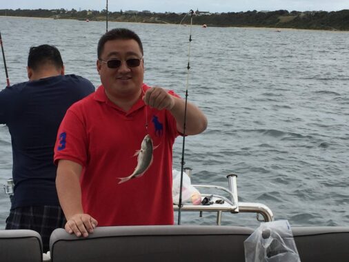 Man holding a fish on a boat during winter fishing in Melbourne.