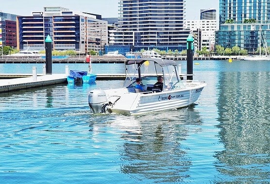 Motorboat on Melbourne waterway with city skyline in background.