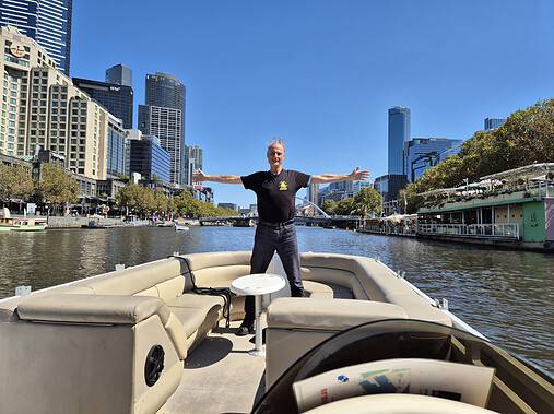Man standing aboard a Boat4Hire Spaceship boat on the Yarra River with Melbourne skyline behind him