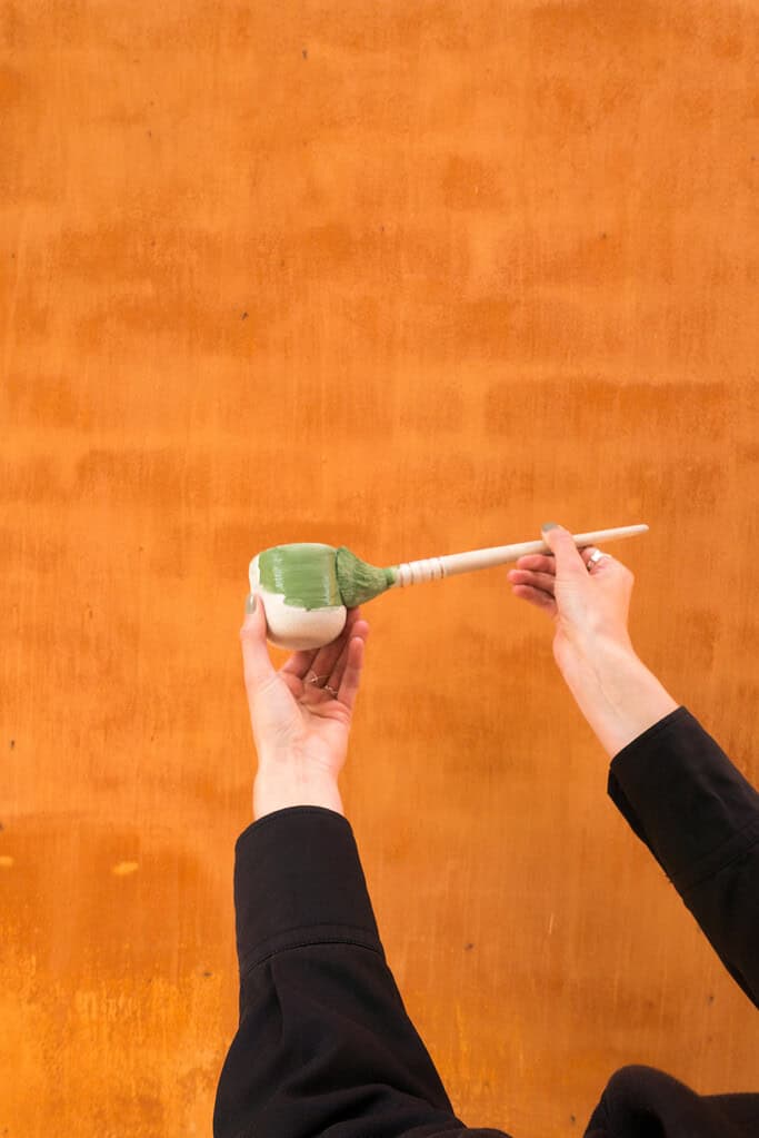 Person holder en grøn og hvid skål med en ske mod en orange baggrund.