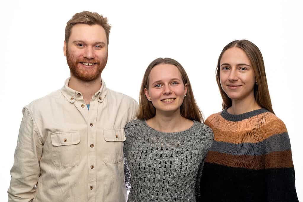 Tre personer smiler og står sammen mod en hvid baggrund.