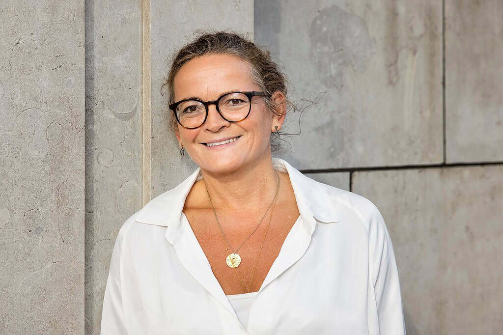 Kvindelig professionel med briller smiler foran betonvæg.