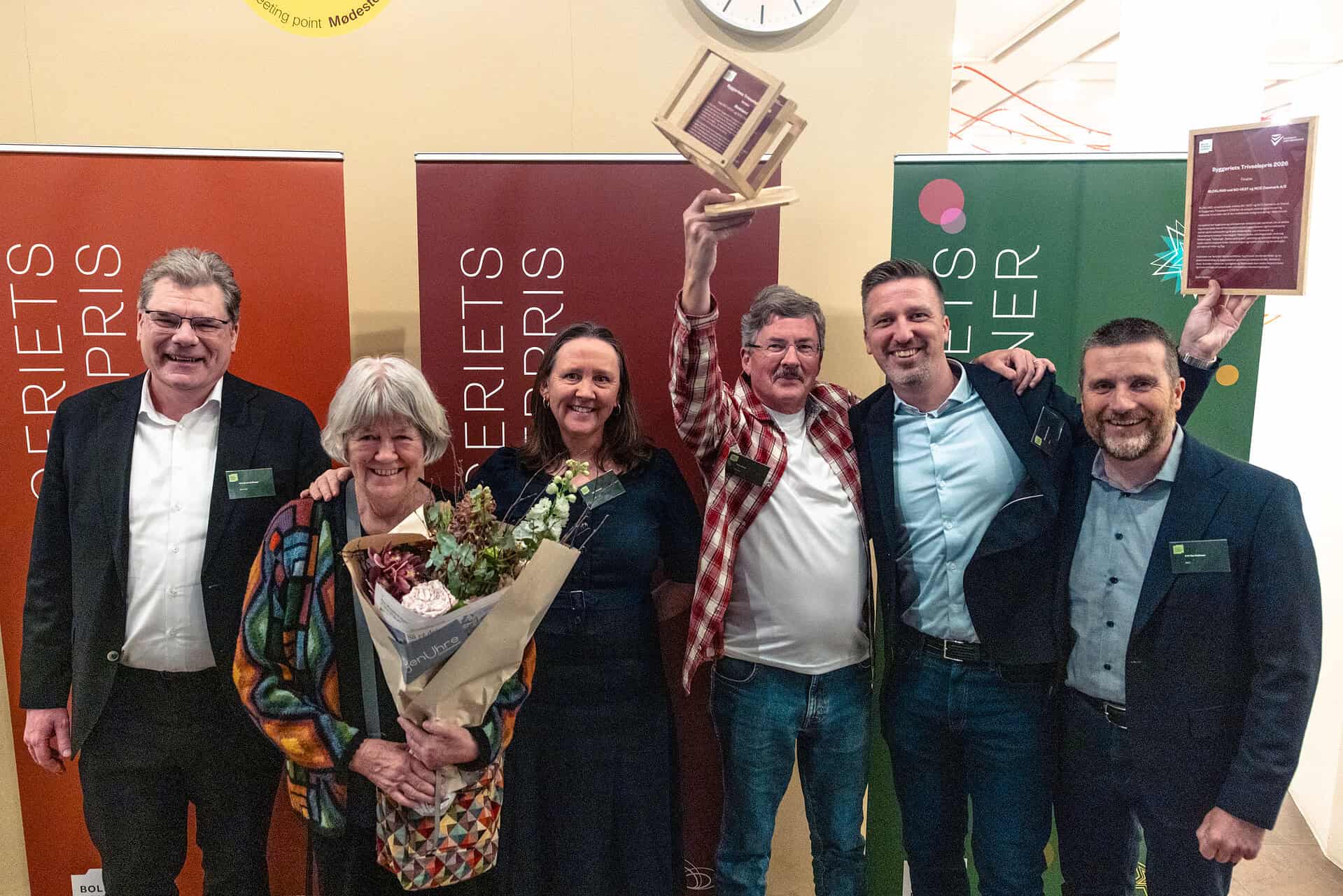 Vindere af Byggeriets Trivselspris 2023 med trofæ og blomster.