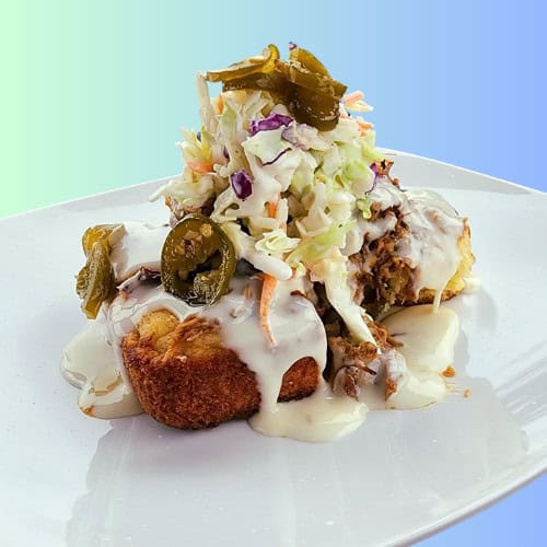 Southern Comfort Cornbread Sandwich topped with coleslaw and jalapeños on a white plate.