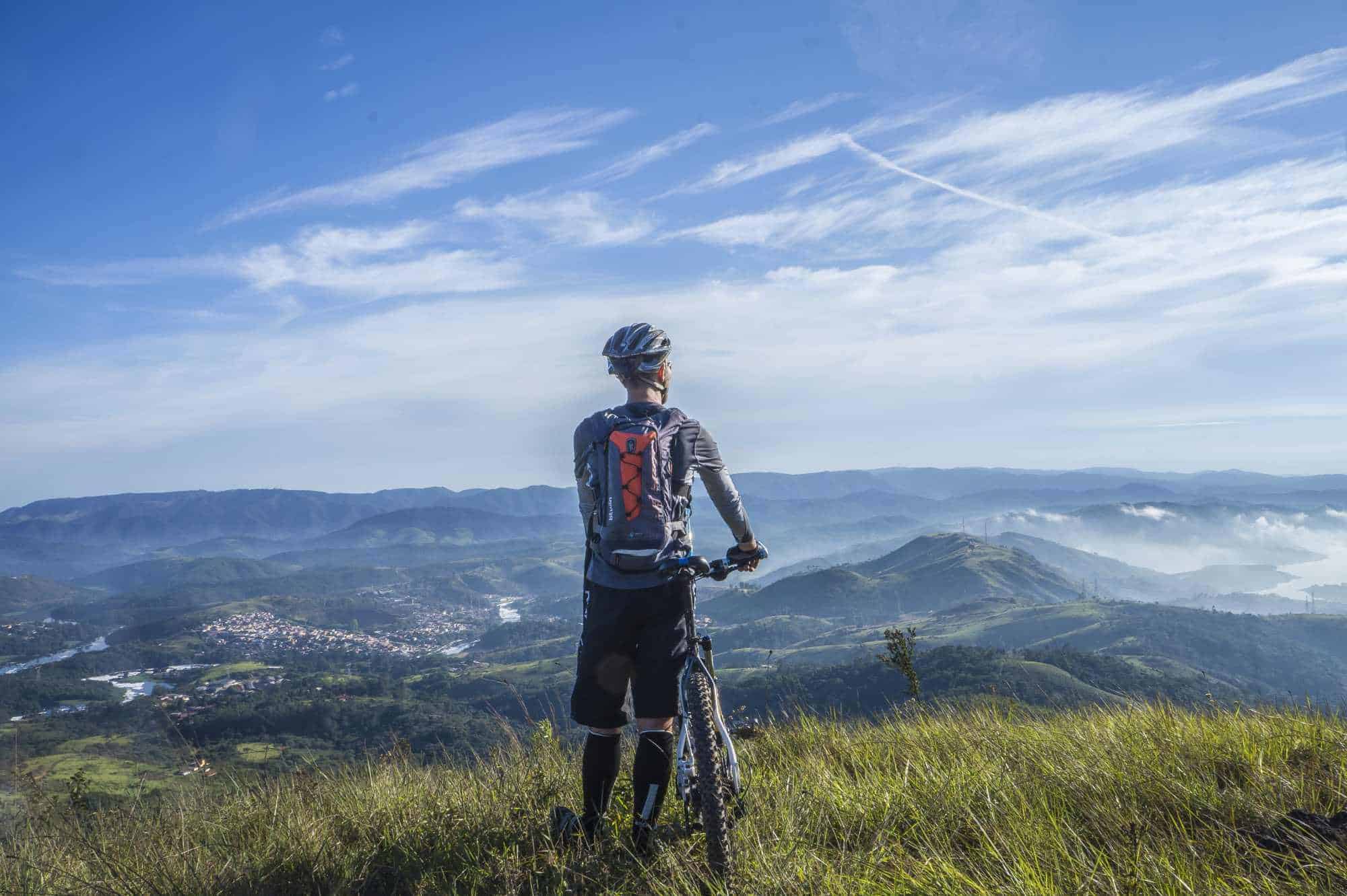 Ein Mountainbiker steht auf der Wiese eines Berges und blickt ins Tal