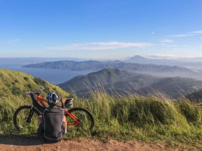 Ein Mountainbiker sitzt auf der Wiese eines Berges und blickt ins Tal