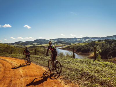 Zwei Mountainbike Fahrer fahren einen unbefestigten Weg hinab. Im Hintergrund ist eine hügellige Landschaft