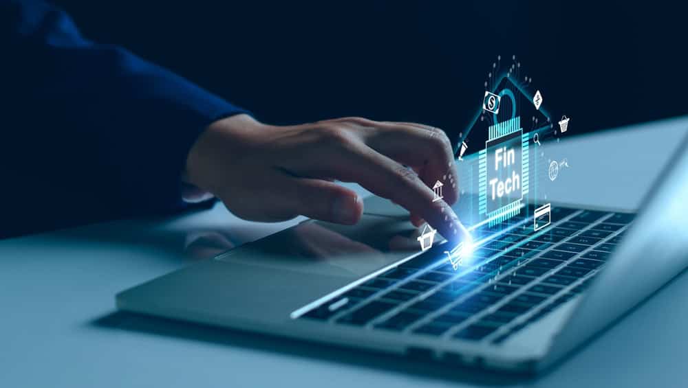 Person using laptop with digital FinTech icons and hologram effects.