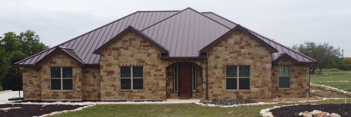 Front view of a single-story, light-brown stone house with a dark reddish-brown metal roof in San Antonio, TX