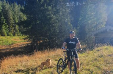 Mann mit Fahrrad und Hund in Natur bei Bergkulisse.