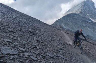 Mountainbiker auf steilem, felsigem Abhang in alpiner Landschaft.