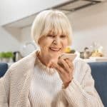 Comfortable elderly woman smiling while using her smartphone at home, representing legal assistance and support for seniors from Farr Law Firm.