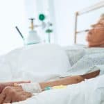 Elderly patient receiving medical care in hospital bed with IV infusion, healthcare and legal support concept.