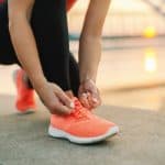Runner tying shoelaces before morning run outdoors at sunrise; athletic woman preparing for exercise in activewear; fitness motivation and healthy lifestyle.