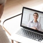 Licensed medical professional engaging in telehealth consultation on laptop.