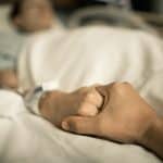 Injured patient holding hand with visitor in hospital bed for emotional support and care.