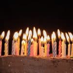 Chocolaty birthday cake with lit colorful candles on a dark background, celebrating a special occasion.