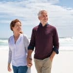 A senior couple walking hand-in-hand on the beach, enjoying a sunny day by the ocean, representing peaceful retirement and legal support for seniors.