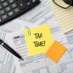 Tax deadline paperwork with pen, calculator, and memo note reading "Tax Time" on financial documents.