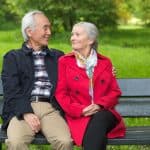 Comfortable elderly couple sitting on park bench, enjoying peaceful moment outdoors in a green setting.
