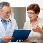 Medical consultation between a healthcare professional and an elderly patient discussing health concerns in a clinic.