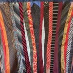 Lyrich neckties with various patterns in red, black, orange, and gold, hanging in a row for sale or display.