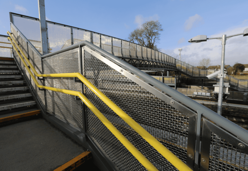 Framed woven wire mesh with yellow handrail at train station