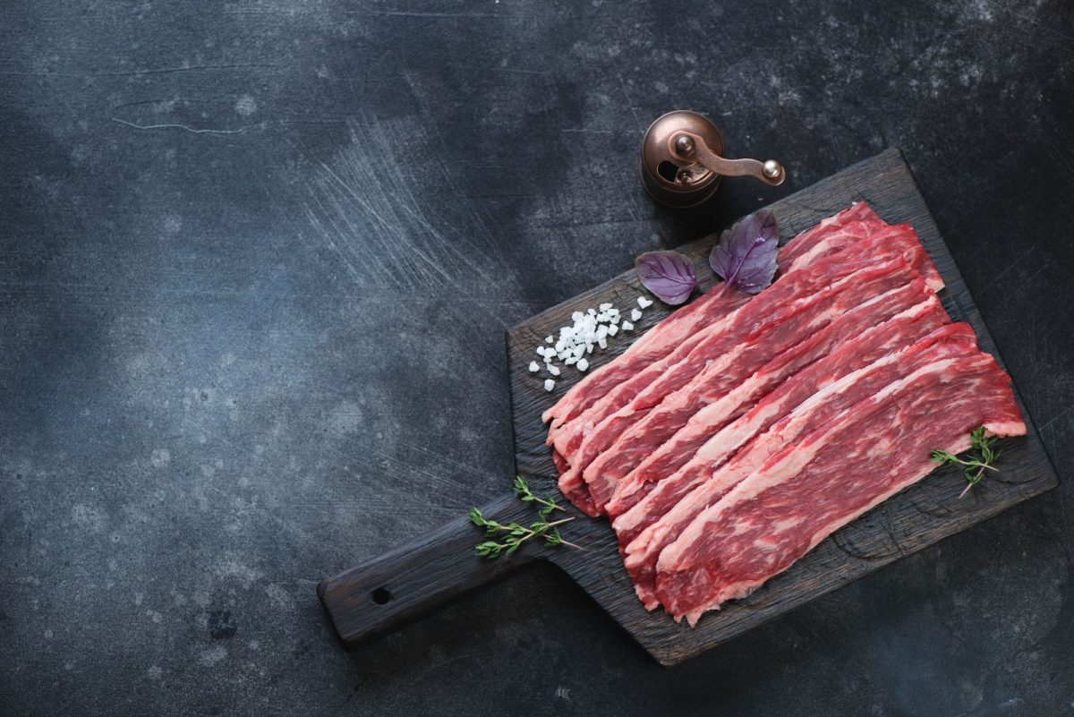 A detailed image of raw beef slices on a dark cutting board with herbs and salt, highlighting organi.