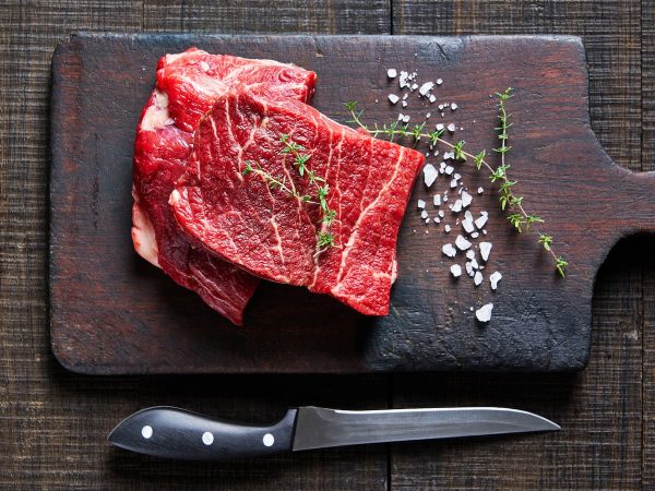 Fresh grass-fed beef steaks on a rustic wooden board with sea salt and thyme, emphasizing natural, o.